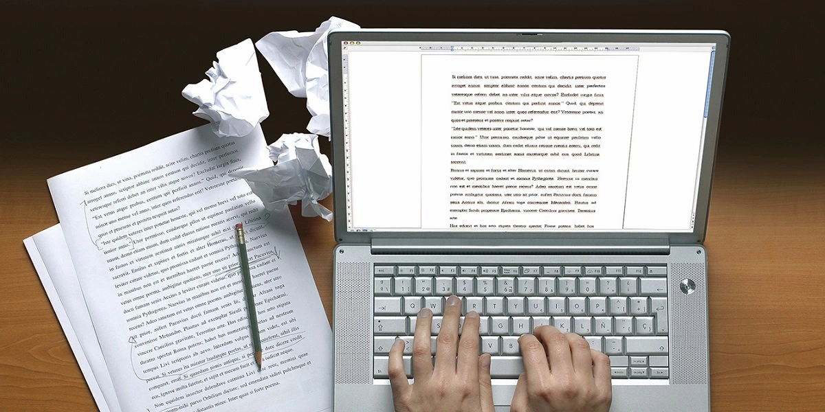 imagem com uma pessoa digitando em um notebook e uma folha de papel escrita com um lápis sobre ela